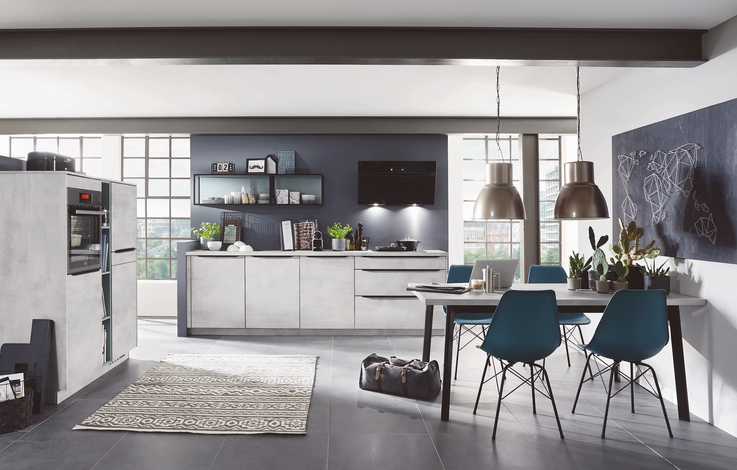 Industrial-style kitchen with concrete-look cabinets, a blue dining table and chairs, and large windows. A world map is drawn on the wall.