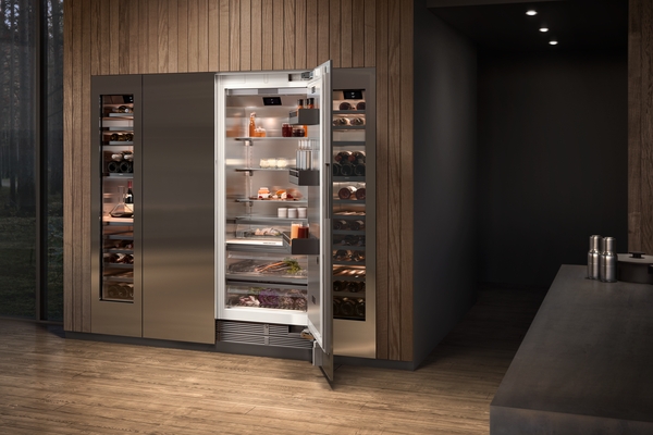 A modern, stainless steel Gaggenau refrigerator and wine cooler combination. The refrigerator door is open, revealing organized shelves stocked with various food and drink items.