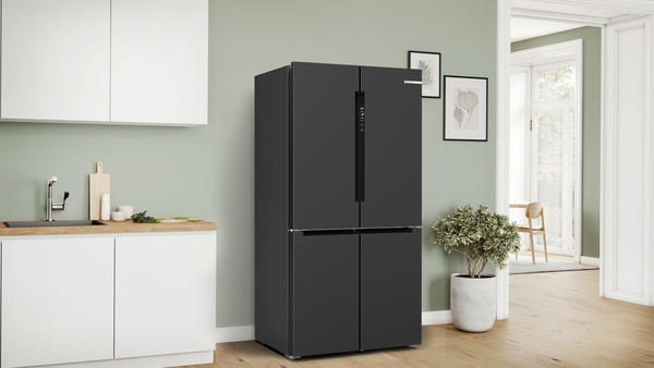 A matte black four-door Bosch refrigerator standing in a contemporary kitchen with light green walls and wooden floors.