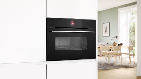 Black built-in Bosch oven with a stainless steel handle and a red indicator light, installed in a modern white kitchen.