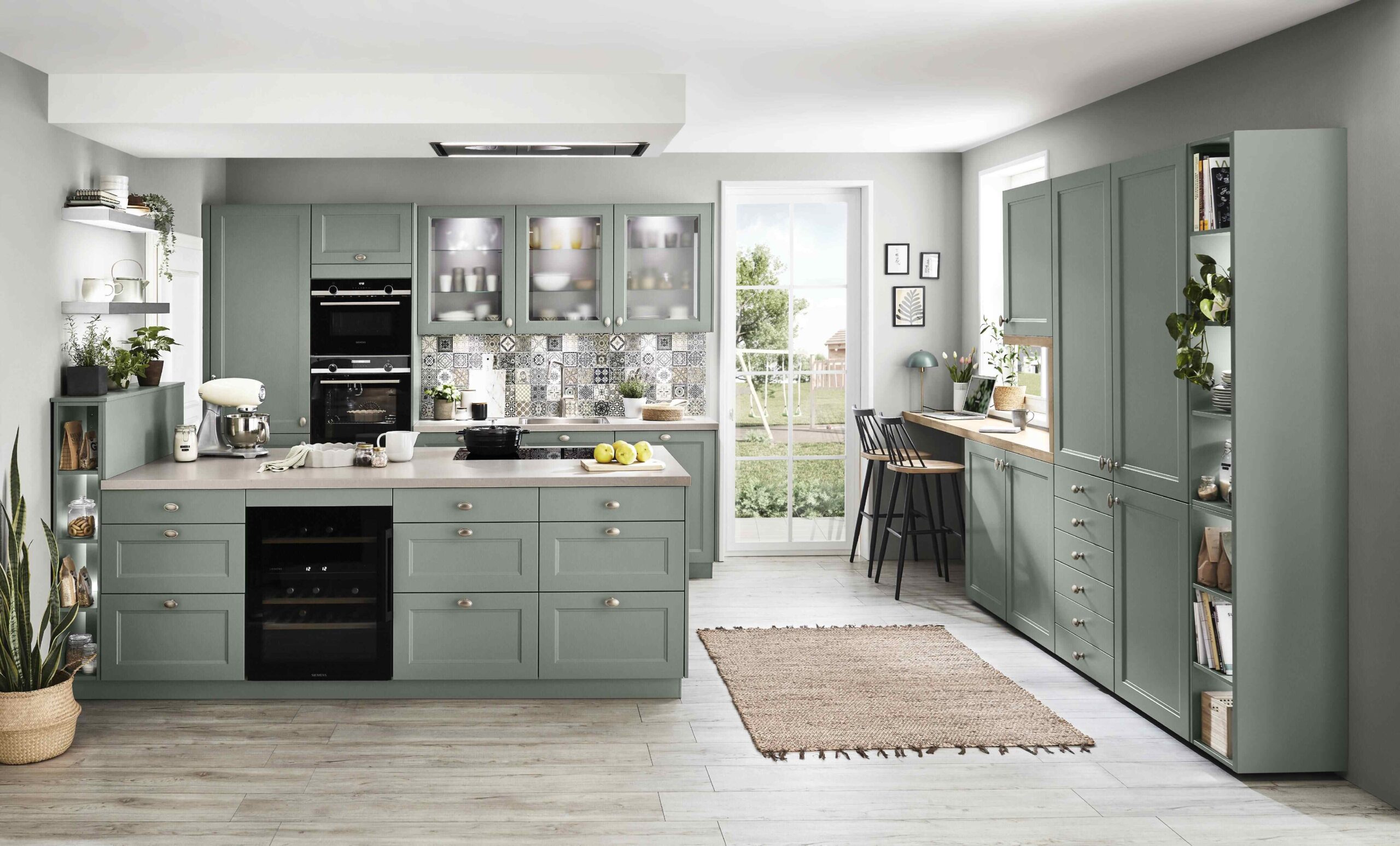 Spacious green cottage-style kitchen with a large island, glass-fronted upper cabinets, and a patterned tiled backsplash.