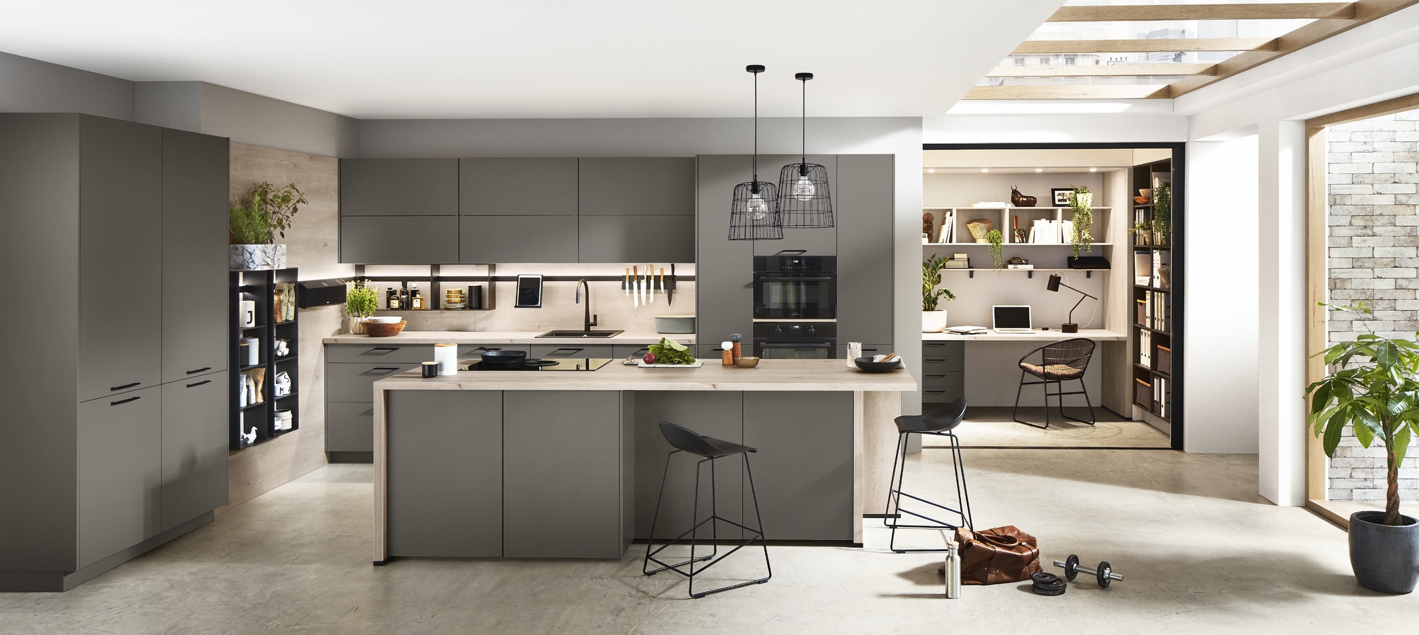 Modern gray kitchen with a large island, bar stools, and an integrated home office area with a desk and shelving.