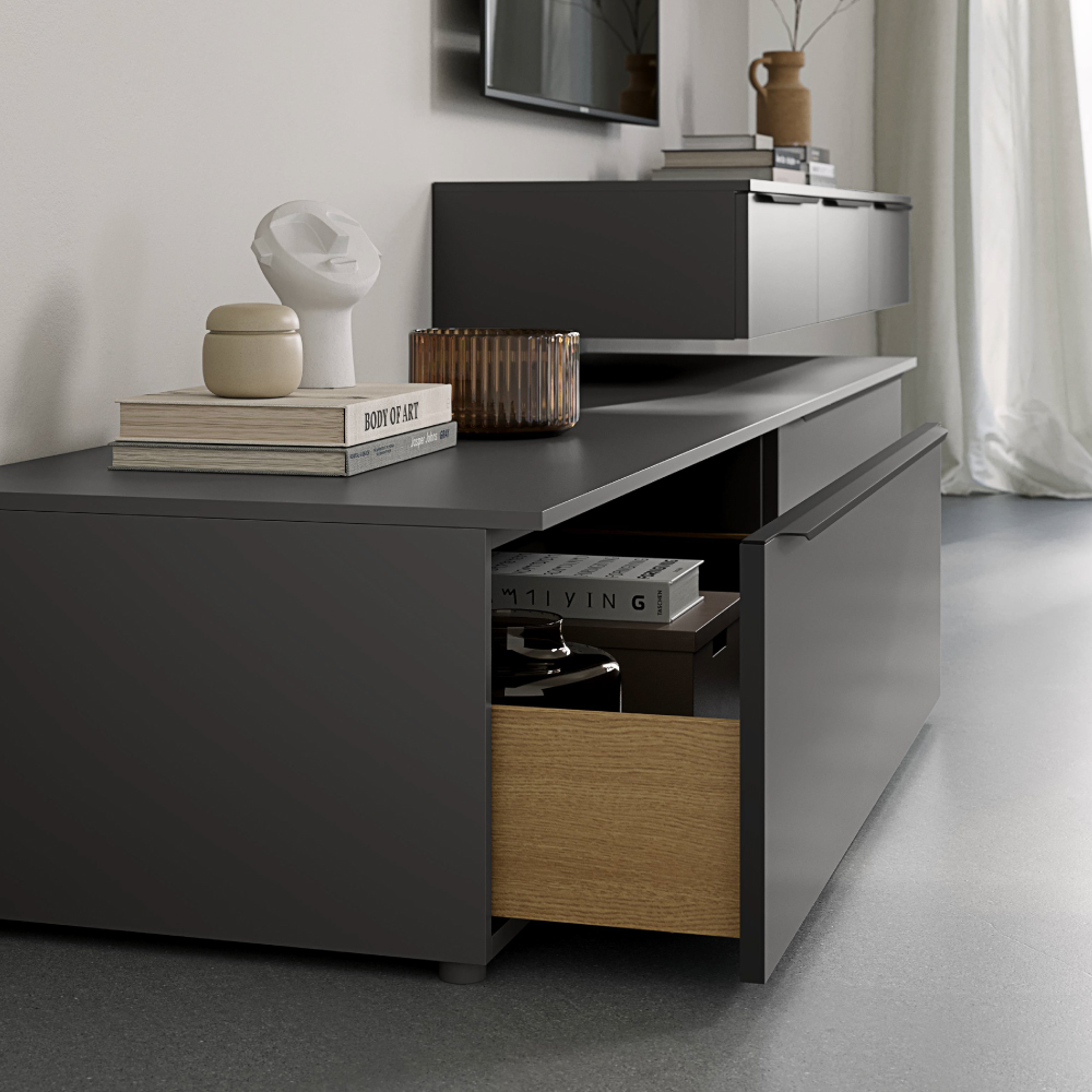 Modern gray media console with an open drawer revealing a light wood interior. Books and decorative objects are placed on top.