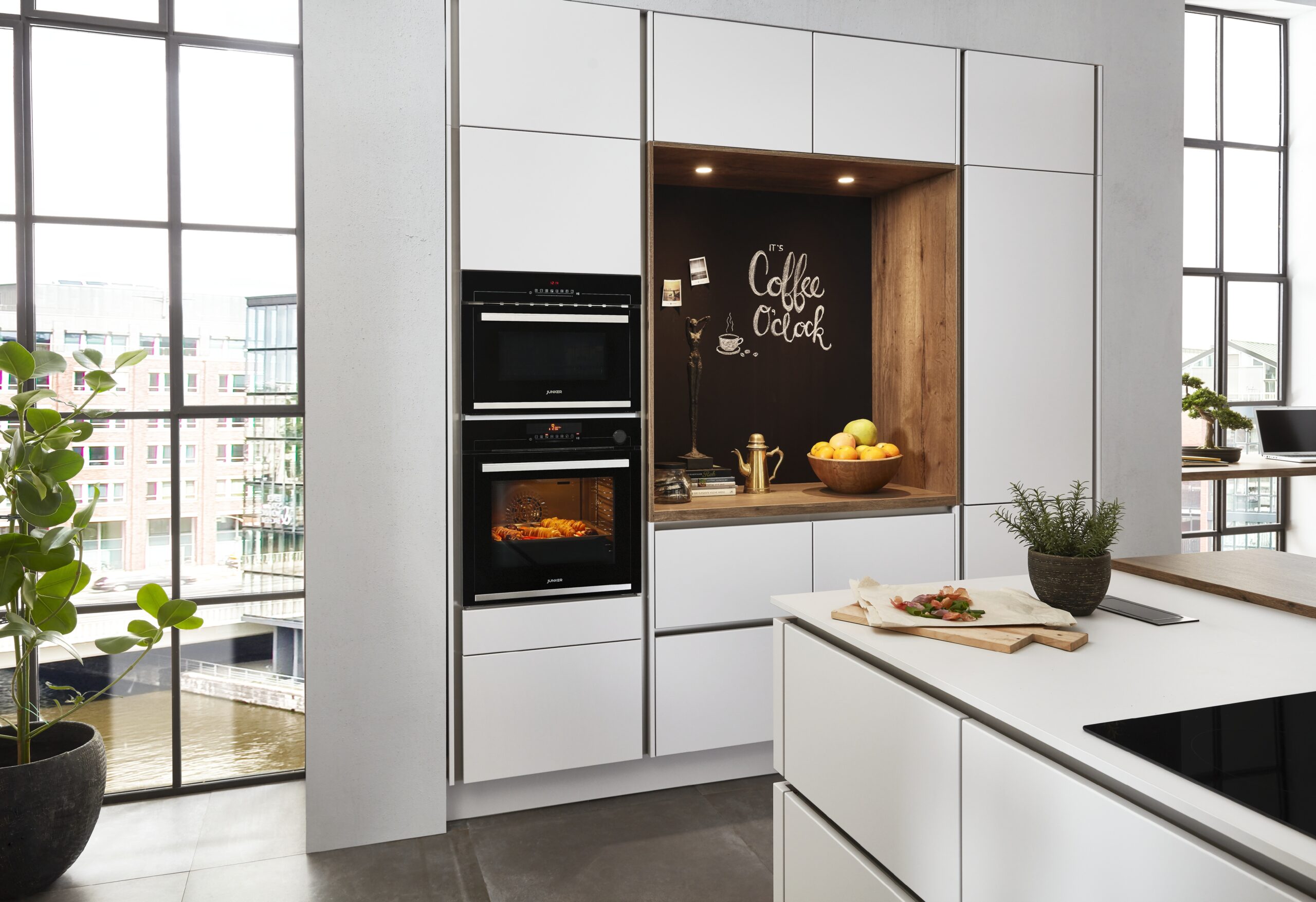 White modern kitchen with a double oven and a chalkboard wall. A kitchen island is partially visible.