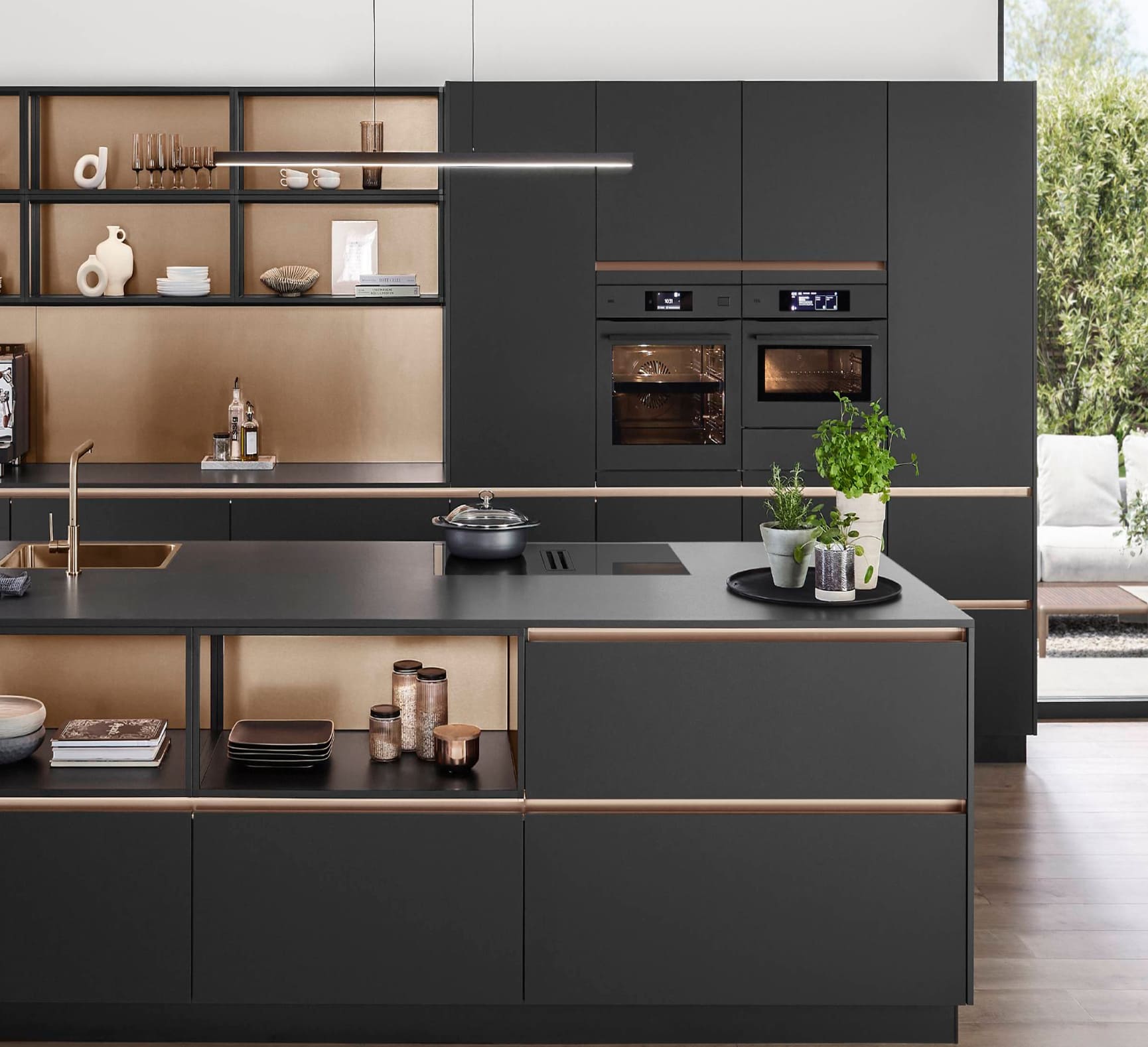 Sleek black kitchen with gold accents, featuring a large island, open shelving, and black appliances. A window offers a view of the outdoors.