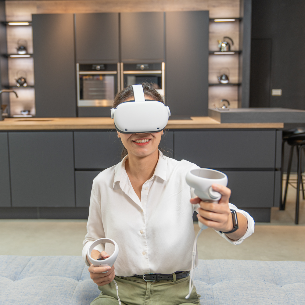 A woman smiles while using a VR headset and controllers in a modern kitchen, likely visualizing a design.