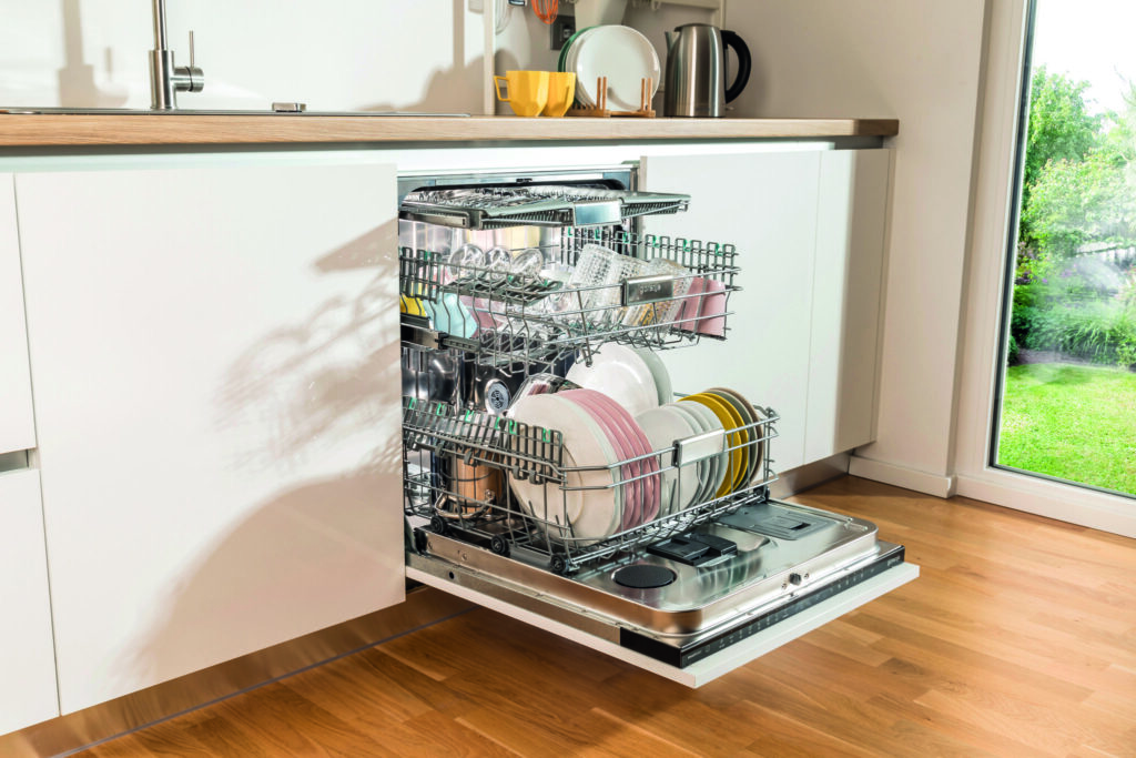 Open Gorenje dishwasher filled with dishes and glassware in a modern white kitchen.