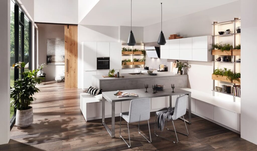 This modern white kitchen features built-in kitchen furniture, seamlessly integrating a dining area into the design. Vertical planters add a touch of nature.