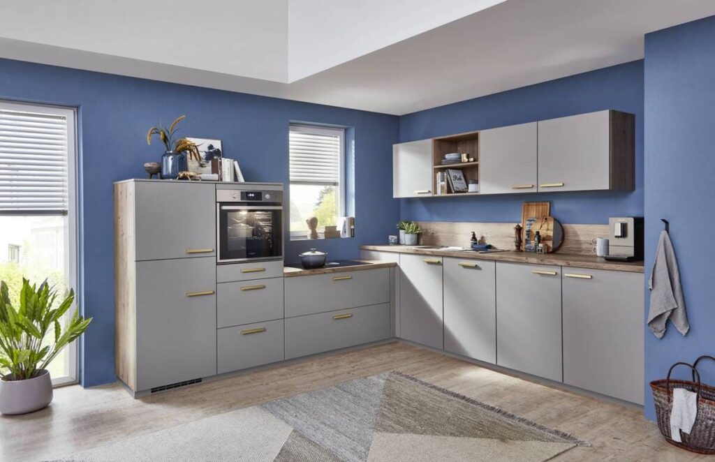 A stylish kitchen with gray cabinets and gold handles accented by a blue wall backdrop.