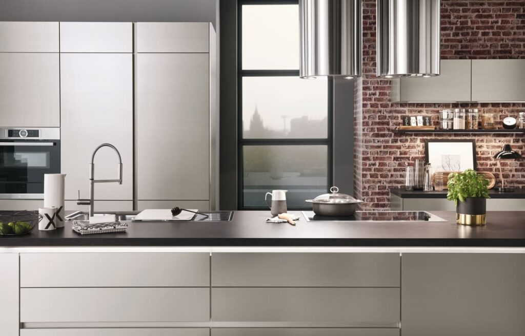 A modern German kitchen with sleek, light cabinetry and an industrial-style brick wall.