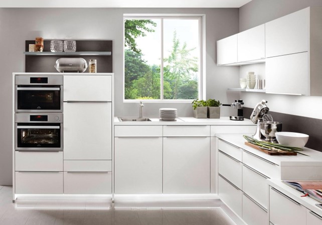 A bright, minimalist white kitchen with integrated appliances, showcasing the clean lines and reflective surfaces often achieved when selecting the best material for kitchen cabinets.